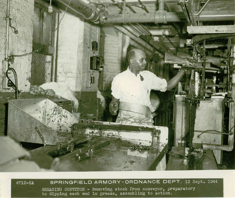 A worker on the greasing conveyer, removing stocks to get ready for assembling to action.